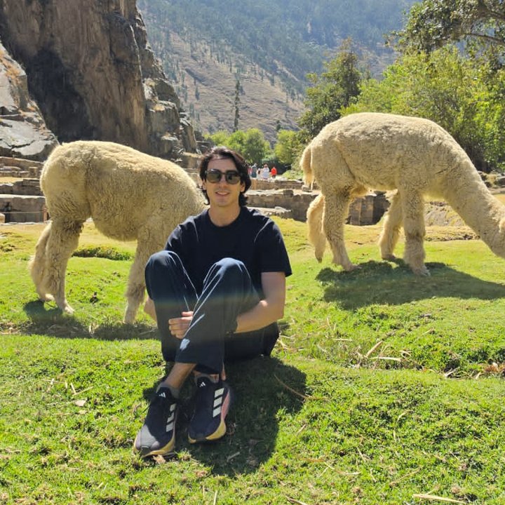 Manuel Quintero sitting on the grass between two grazing alpacas